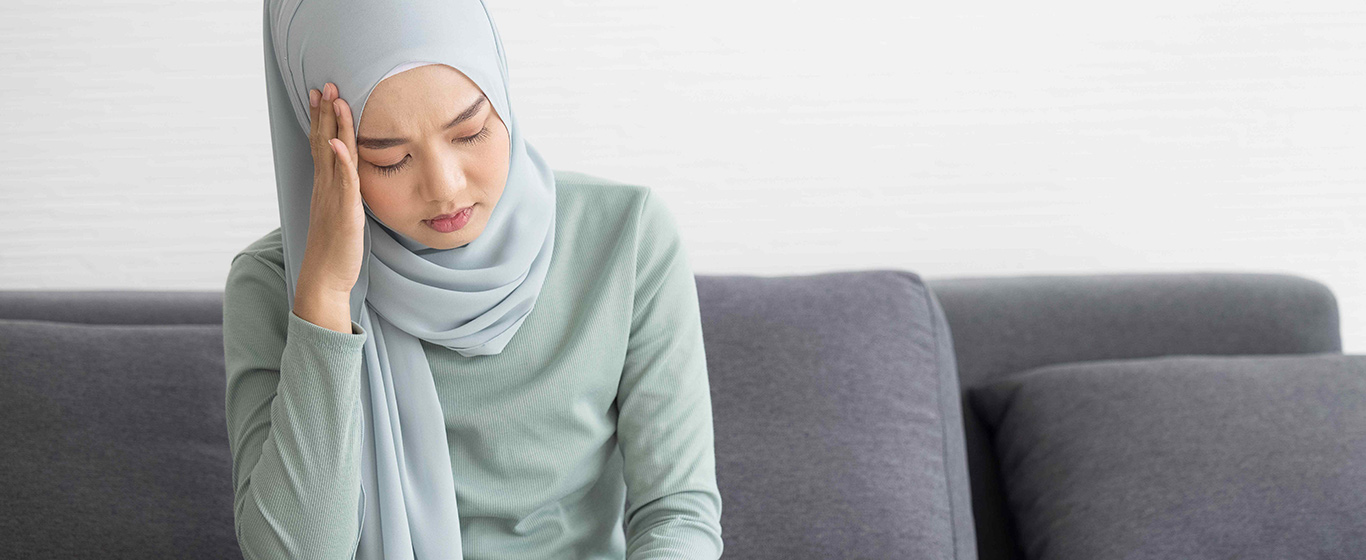 wanita muslim duduk sambil memegang kepala