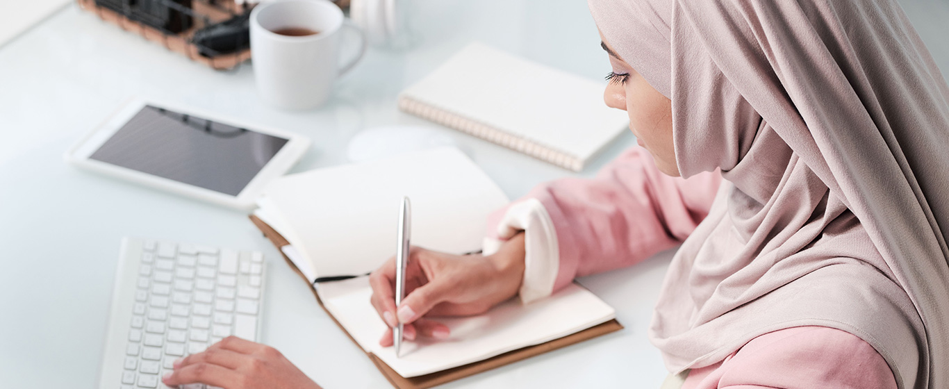 wanita berjilbab sedang menulis di buku catatan